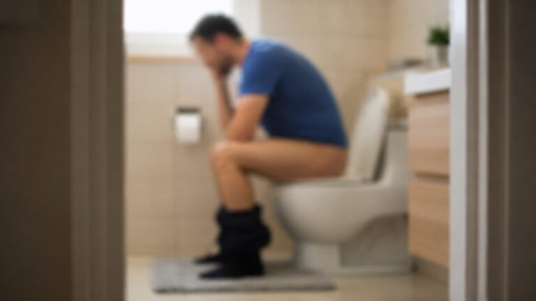 Muškarac sedi na WC šolji u zamućenoj sceni kupatila zbog problema sa pražnjenjem creva.